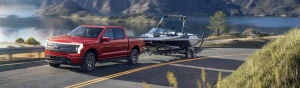 Front side view of F-150 Lightning pulling. a boat with a lake and moutnains in the background