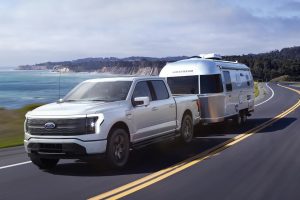 Front side view of F-150 Lightning pulling a camper in front of body of water